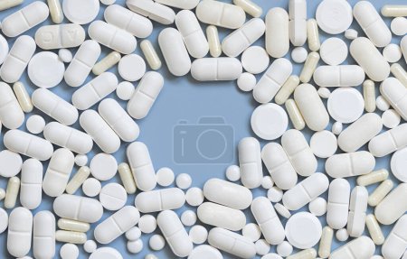 Photo for Mix of white medical capsules and pills with copy space in the middle on light blue top view. Medicinal treatment. Taking dietary supplements and vitamins. Assorted pharmaceutical products - Royalty Free Image