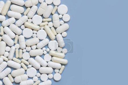 Photo for Mix of white medical capsules and pills on light blue top view, copy space. Medicinal treatment. Taking dietary supplements and vitamins. Assorted pharmaceutical products - Royalty Free Image