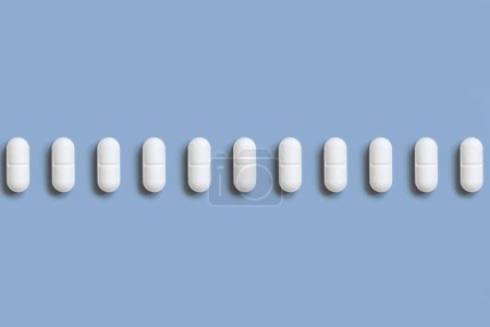 Foto de Mezcla de píldoras médicas blancas en una línea en la vista superior azul claro. Medicina preventiva y salud, suplementos dietéticos y vitaminas. Surtido de cápsulas de medicamentos farmacéuticos - Imagen libre de derechos