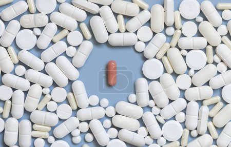 Photo for Mix of white medical capsules and pills with one pink capsule in the middle on light blue top view. Medicinal treatment. Taking dietary supplements and vitamins. Assorted pharmaceutical products - Royalty Free Image