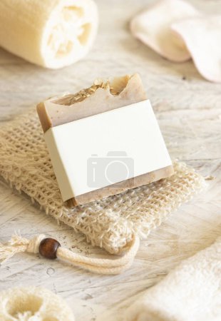 Photo for Beige handmade soap bar with blank label on soap saver bag on wooden table, packaging mockup, copy space. Natural herbal products for face and body care - Royalty Free Image