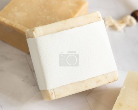 Photo for Beige handmade soap bar with blank label on white marble, packaging mockup, copy space. Natural herbal products for face and body care - Royalty Free Image
