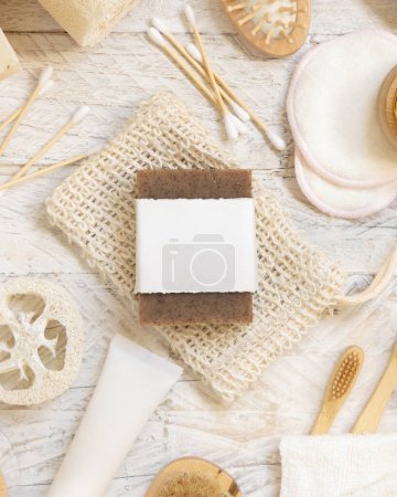 Photo for Organic handmade beige soap bar with blank label on soap saver bag near hygiene Items - natural sponges and brush, bamboo toothbrushes and cotton swabs, top view,  mockup - Royalty Free Image