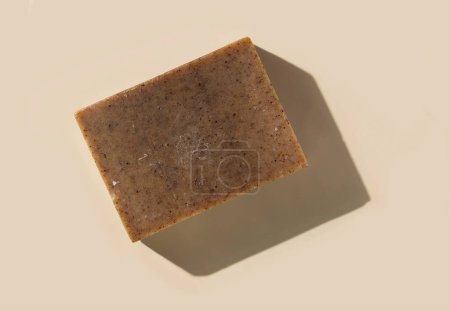 Photo for Natural herbal brown soap bar on light beige top view, hard shadows. Hygiene products for Spa and skin care. Using organic handmade soap for everyday bathroom routine - Royalty Free Image