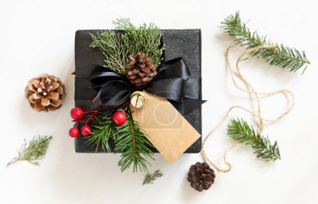 Téléchargez les photos : Cadeau noir avec étiquette cadeau vertical de Noël, branches de sapin, cônes de pin et décorations de vacances, vue de dessus. Composition d'hiver avec étiquette vierge Mockup, espace de copie, vue du dessus - en image libre de droit