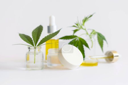 Photo for Cream jar and pipette with CBD oil near green cannabis leaves closeup on white. Organic skincare and healthcare products. Alternative medicine concep - Royalty Free Image