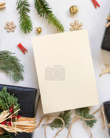 Téléchargez les photos : Carte en papier entre décor de Noël, coffrets cadeaux noirs et branches de sapin vert vue du dessus. Modélisation verticale de la carte blanche, pose à plat, espace de copie. Noël ou Nouvel An vœux de vacances - en image libre de droit
