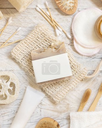 Photo for Organic handmade beige soap bar with blank label on soap saver bag near hygiene Items - natural sponges and brush, bamboo toothbrushes and cotton swabs, top view,  mockup - Royalty Free Image
