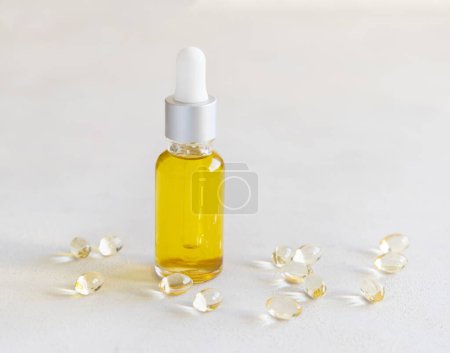 Foto de Aceite amarillo en un frasco de gotero y cápsulas en una mesa blanca de cerca. Medicina preventiva y salud, suplementos dietéticos y vitaminas - Imagen libre de derechos