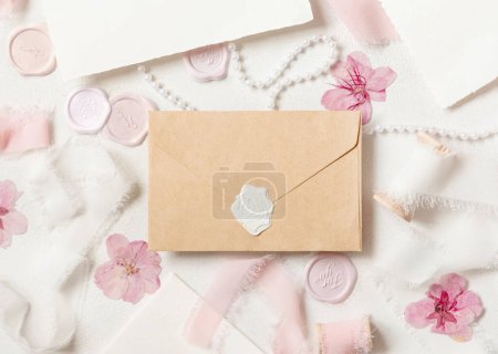 Photo for Sealed envelope near pink decorations, seals and silk ribbons on white table top view,  wedding mockup. Romantic scene with horizontal blank card flat lay. Valentines, Spring or Mothers day concept - Royalty Free Image