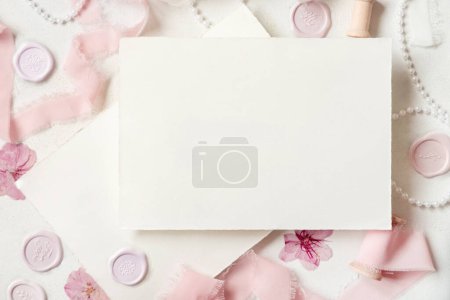 Photo for Paper card near pink decorations, seals and silk ribbons on white table top view,  wedding mockup. Romantic scene with horizontal blank card flat lay. Valentines, Spring or Mothers day concept - Royalty Free Image