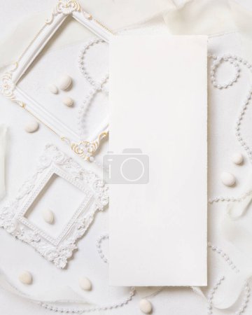 Photo for Blank paper card near white frames, pearls, pebbles and silk ribbons on white table top view,  wedding menu mockup. Romantic scene with Vertical card flat lay. Valentines, Spring or Mothers day concept - Royalty Free Image