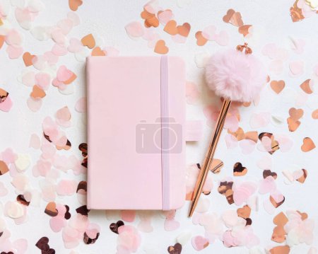 Foto de Cuaderno rosa de tapa dura cerca de corazones y bolígrafo de piel en la vista superior de la mesa blanca. Maqueta romántica femenina para boda, San Valentín, Primavera o día de la madre - Imagen libre de derechos