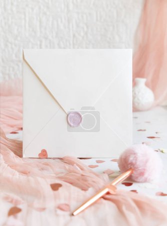 Photo for Sealed square envelope near fur pen, pink decorations, hearts and silk tulle on white table close up. Romantic mockup for Wedding, Valentines, Spring or Mothers day stationery - Royalty Free Image