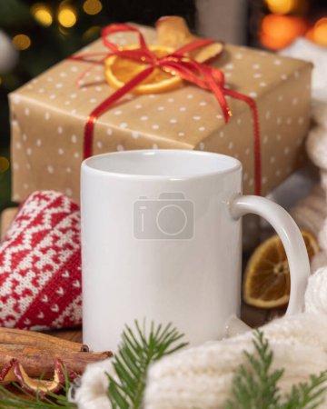 Téléchargez les photos : Tasse à café blanche près du cadeau de Noël, coeur confortable et pull près contre les lumières du sapin de Noël et cheminée en feu, espace de copie. Chaleureux hiver famille atmosphère maquette, magique Holiday tim - en image libre de droit