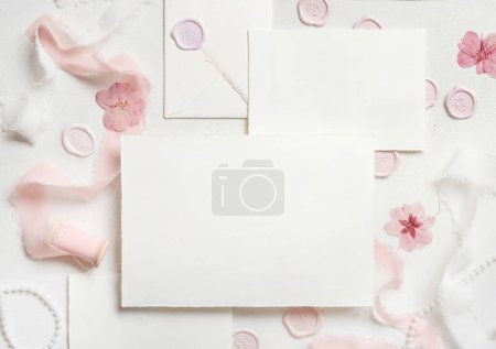 Photo for Cards set near pink decorations, seals and silk ribbons on white table top view,  wedding mockup. Romantic scene with horizontal blank card flat lay. Valentines, Spring or Mothers day concept - Royalty Free Image