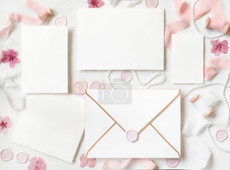 Photo for Paper cards set with envelope near pink decorations, seals and silk ribbons on white table top view,  wedding mockup. Romantic scene with blank cards flat lay. Valentines, Spring or Mothers day - Royalty Free Image