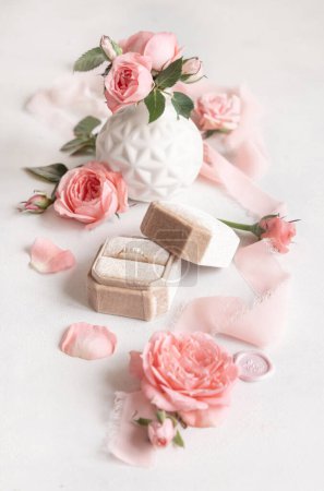 Foto de Anillo de compromiso en una caja de terciopelo crema cerca de rosas rosadas claras, brotes y cintas de seda de cerca, preparaciones románticas de boda. Concepto de propuesta de matrimonio, escena de San Valentín - Imagen libre de derechos