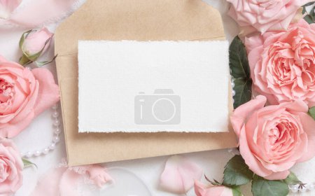 Photo for Blank card and envelope near light pink roses and silk ribbons on white table top view,  wedding mockup. Romantic flat lay with horizontal card and pastel decor - Royalty Free Image