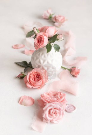 Téléchargez les photos : Roses rose clair dans un vase, pétales et bourgeons sur table blanche close up, concept romantique et de mariage, scène de la Saint-Valentin, backgroun ambiance printemps - en image libre de droit