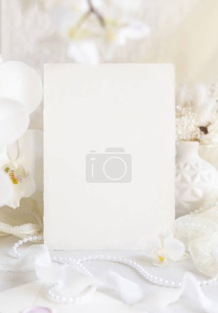 Photo for Card near white orchid flowers and decor close up,  mockup. Pastel romantic scene with vertical blank card for Wedding, Valentines, Spring or Mothers day stationery - Royalty Free Image