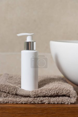 Foto de Blanco una botella de la bomba cerca del lavabo en la toalla doblada en la encimera de madera en el baño beige, primer plano, maqueta cosmética. Composición mínima para el embalaje de la marca - Imagen libre de derechos
