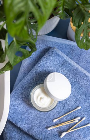 Photo for Opened cream jar with blank white lid and bamboo cotton swabs on blue towels near basin and green monstera blue countertop, top view, mockup.  Lifestile scene with skincare beauty product in bathroom - Royalty Free Image
