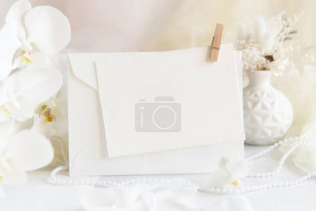 Photo for Card and envelope near white orchid flowers and decor close up,  mockup. Pastel romantic scene with horizontal blank card for Wedding, Valentines, Spring or Mothers day stationery - Royalty Free Image