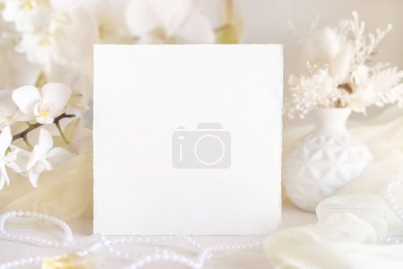 Foto de Tarjeta cerca de flores de orquídea blanca y decoración de cerca, maqueta. Pastel romántica escena con tarjeta en blanco cuadrado para la boda, San Valentín, Primavera o Madres papelería día - Imagen libre de derechos