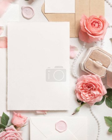 Photo for Blank card near light pink roses, engagement ring in a box and silk ribbons on white table top view,  wedding mockup. Romantic flat lay with vertical card and pastel decor - Royalty Free Image