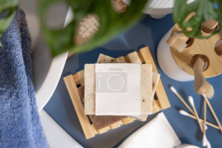 Photo for Soap bar with blank label on blue bathroom countertop near monstera plant and basin top view, packaging mockup, copy space. Natural hygiene products and cosmetics - Royalty Free Image