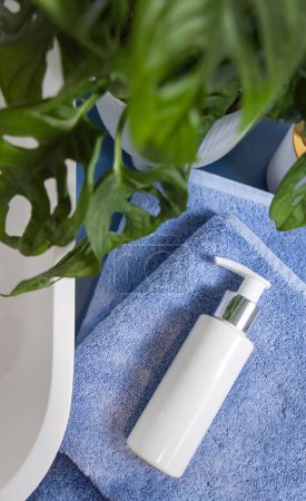 Photo for White one pump cosmetic bottle on folded blue towels near basin and green monstera, top view, mockup.  Lifestile scene with skincare beauty product in bathroom - Royalty Free Image