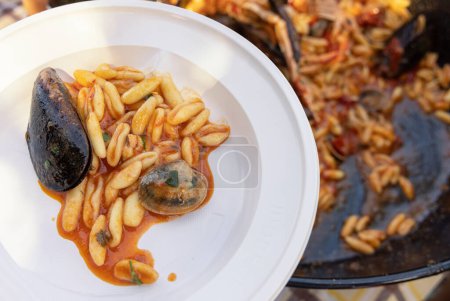 Plastikteller Cavatelli mit schwarzen Miesmuscheln, Garnelen und Tomaten in einer Pfanne aus nächster Nähe. Sommer-Familienpicknick mit italienischen Meeresfrüchten 