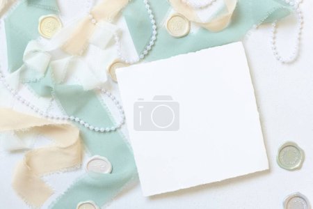 Photo for Square card near  light green and beige decor and silk ribbons on white table top view,  Wedding mockup. Romantic scene with blank card. Valentines, Spring or Mothers day stationery - Royalty Free Image