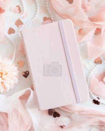 Photo for Pink hardcover notebook near hearts and romantic pink decor on white table top view. Romantic mockup for Wedding, Valentines, Spring or Mothers day - Royalty Free Image