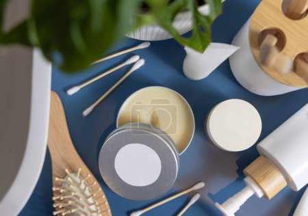 Photo for Opened body butter jar with blank round label on lid on blue bathroom countertop near monstera plant and basin top view, packaging mockup, copy space. Natural personal care cosmetics and products - Royalty Free Image