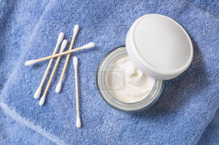 Photo for Opened cream jar with white lid near cotton swabs on blue towel in bath top view, cosmetic mockup.  Lifestile scene with skincare product, beauty routine - Royalty Free Image