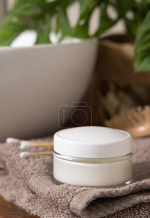 Photo for Cosmetic cream jar with blank white lid on beige folded towels near basin and green monstera on wooden countertop, close up, mockup.  Lifestile scene with skincare product in bathroom - Royalty Free Image