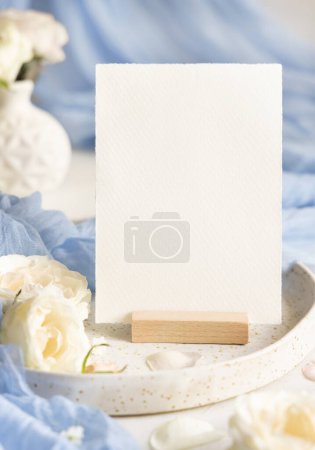 Téléchargez les photos : Carte vierge près de tissu de tulle bleu clair et fleurs crème sur plaque fermer, copier l'espace. Modèle de papeterie de mariage. Lieu de table romantique avec carte de papier verticale et décor pastel - en image libre de droit
