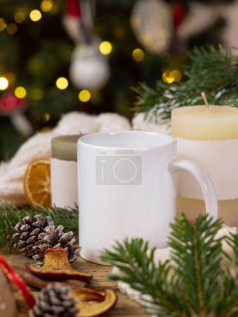 Photo for White coffee mug near Christmas decor, candles and fir twigs close up against Christmas tree lights, copy space. Warm winter family atmospheric mock up, magical Holiday time with a coffe - Royalty Free Image