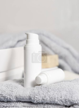 Téléchargez les photos : Bouteilles cosmétiques blanches une pompe sur serviette pliée grise près du lavabo dans la salle de bain close up, maquette cosmétique. Scène de vie moderne avec des produits de soins personnels féminins - en image libre de droit