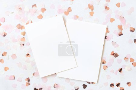 Foto de Tarjetas verticales entre corazones rosados en la vista superior de la mesa blanca. Maqueta romántica para el día de la boda, San Valentín, primavera o madre - Imagen libre de derechos
