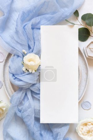 Téléchargez les photos : Carte blanche verticale près du noeud en tissu de tulle bleu clair et des roses crème sur les plaques vue du dessus, espace de copie. Modèle de menu de mariage. Fleurs romantiques et décor pastel - en image libre de droit