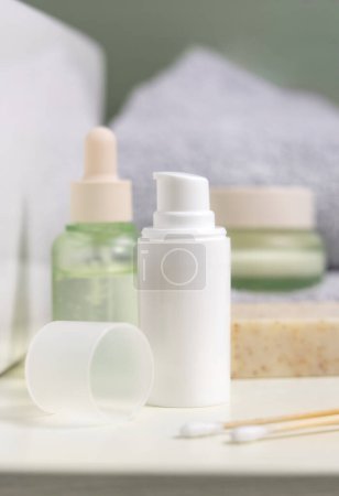 Photo for White one pump cream bottle near soap, cosmetic bottles and jars in bathroom against light green wall, close up, mockup. Daily beauty routine with organic skincare products, spa concept - Royalty Free Image