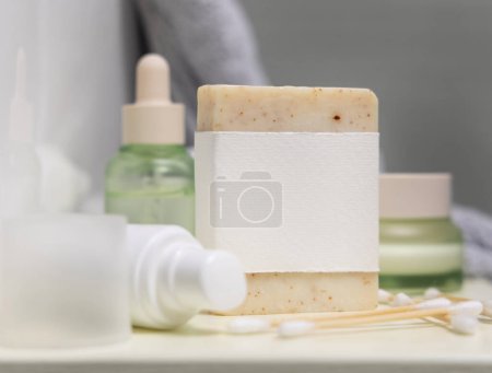 Foto de Barra de jabón con etiqueta en blanco cerca de artículos de cuidado personal y botellas de cosméticos de cerca, maqueta de embalaje, espacio de copia. Productos de higiene natural para la rutina de belleza femenina - Imagen libre de derechos