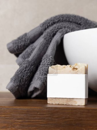 Porte-savon avec étiquette vierge près d'une serviette pliée grise sur le lavabo du récipient sur un comptoir en bois brun dans une salle de bain beige, gros plan, maquette pour l'emballage de la marque. Produit d'hygiène naturel fait main