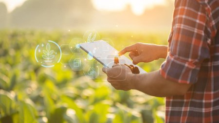 Asian farmer using digital tablet showing smart farming interface icons and light flare sunset effect. Smart and new technology for agriculture business concept.