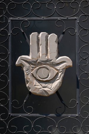 Photo for Haifa, Israel August 20, 2020 Carved rock Hamsa with eye in the palm with black steel frame against a black background in Haifa, Israel. - Royalty Free Image