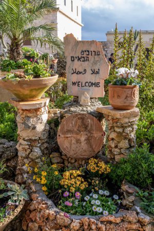 Foto de Haifa, Israel 4 de febrero de 2023 Señal de bienvenida en una roca con una pequeña estatua de María y Jesús, placa de arcilla y plantas decorativas en macetas en el Monasterio Carmalita de Muhraqa en el Monte Carmelo, Haifa, Israel. - Imagen libre de derechos