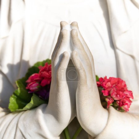 Foto de Primer plano de las manos de oración con flores en ellas de la estatua de la Virgen María en el patio del Monasterio de Muhraqa en el Monte Carmelo en Israel. - Imagen libre de derechos